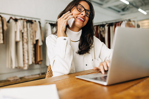 Happy clothing designer speaking on a phone call in her shop