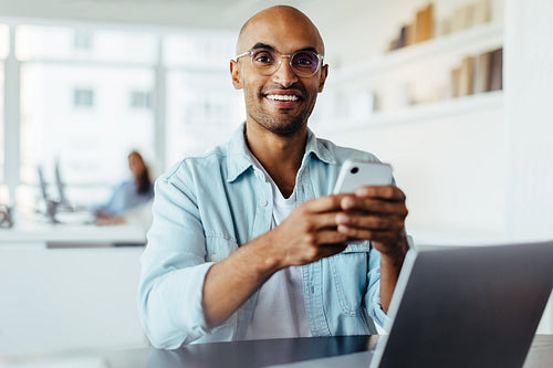 Business man using a smartphone while sitting with a laptop