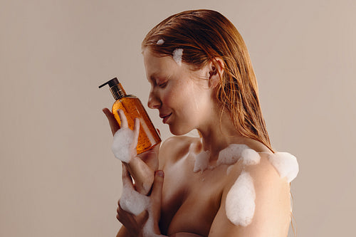 Woman enjoying shampoo foam while holding amber bottle