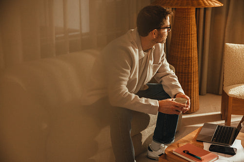 Businessman pauses with coffee beside a laptop in his office workspace