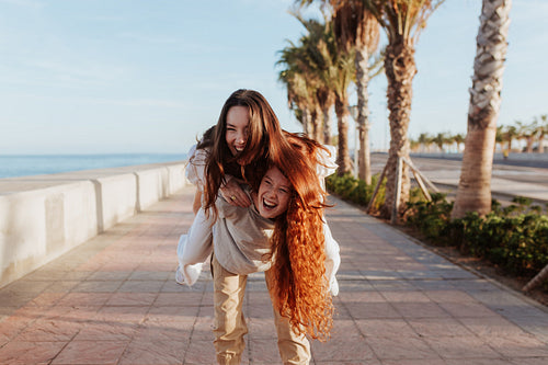 Happy young woman piggybacking her best friend on a promenade