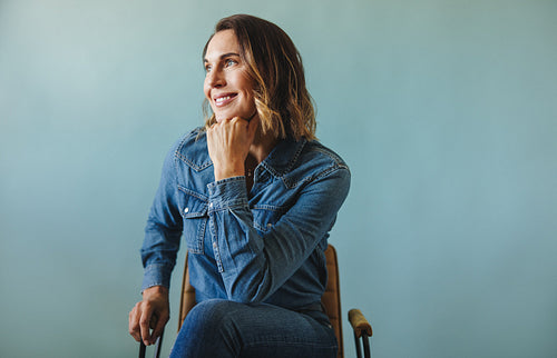 Happy female CEO wearing casual denim and sitting on a chair in studio