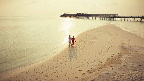 Couple walks on tropical beach at sunset near luxury resort during vacation