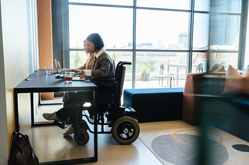 Young professional woman using wheelchair working at desk in modern creative office