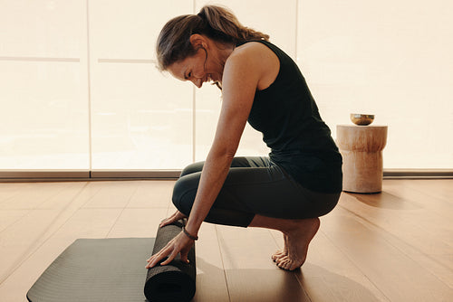 Cheerful senior woman folding up a yoga mat at home