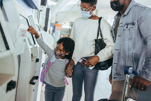 Family in face masks at airport self-service check in machine