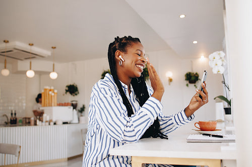 Young businesswoman waving on a video call while working in a coffee shop