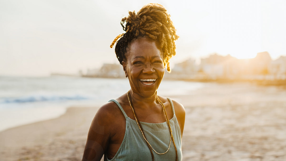 Happy senior African American woman with braids smiling at the beach d ...