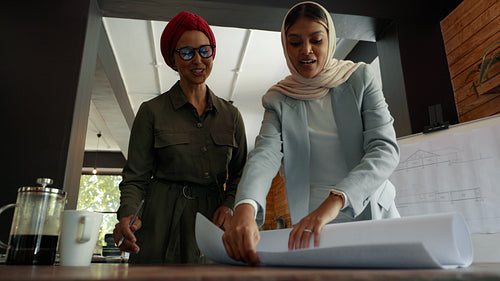 Teamwork in hijabs: Designers in headscarves come together to discuss blueprint drawings in an office