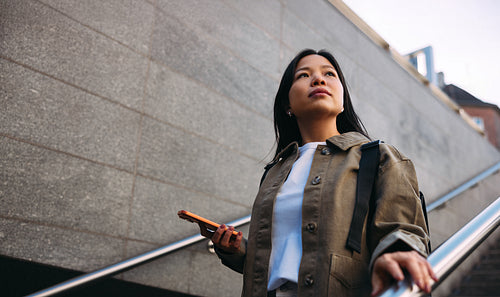 Woman with smartphone looking confident on urban stairway