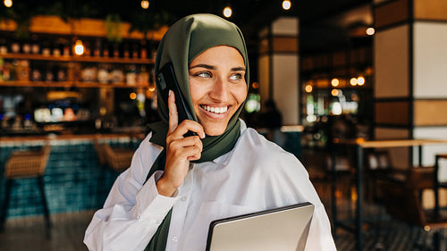 Cheerful Muslim freelancer making a phone call in a cafe