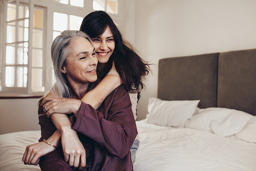 Happy women hugging her mother from behind sitting on bed