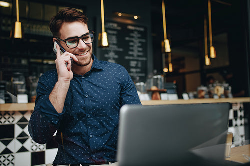 Smiling businessman talking on cell phone while working on laptop