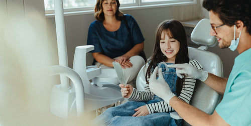 Girl views dental alingers with dentist and mother in clinic