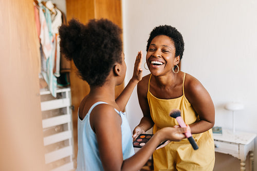 Girl time in the bedroom: Daughter applying makeup on her mom, sharing smiles together