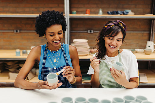 Cheerful female ceramists decorating their handmade ceramic cups