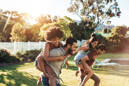 Two happy young men piggybacking their girlfriends