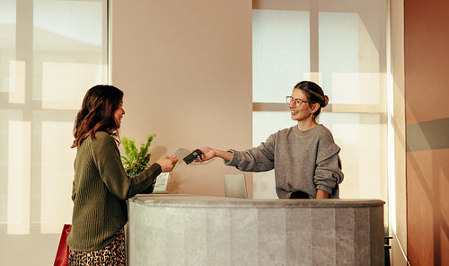Cheerful shop assistant taking a card payment from a female cust
