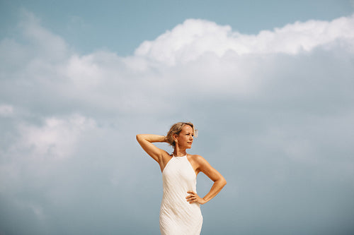 Woman in white dress posing against a blue sky on an overcast day