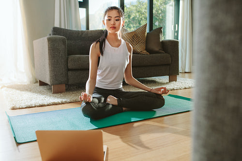 Woman doing yoga while watching instructional videos on laptop