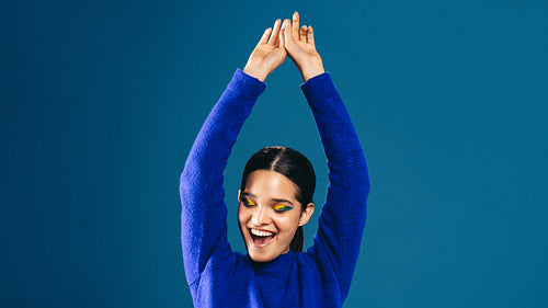 Celebrating her striking style, woman with bold eyeliner cheers in a studio