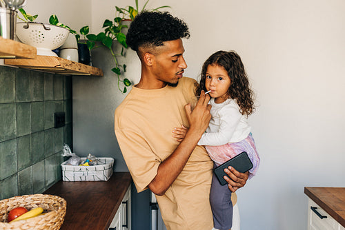 Single dad helping his daughter drink from a glass at home