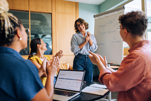 Team members applaud a woman leading a presentation in an office setting