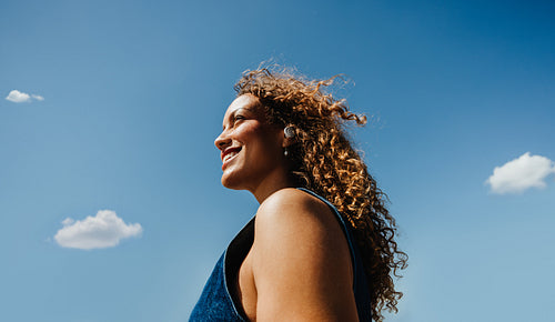 Young woman streams music with earphones against a blue sky