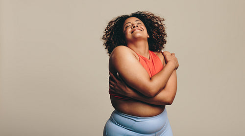 Body confident young woman embracing her body in a studio, expressing self-love