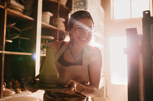 Woman holding a finished clay pot on potters wheel base
