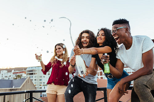 Friends popping a champagne bottle at rooftop party