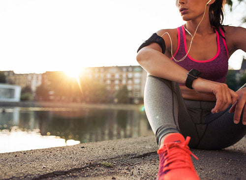 Young woman runner resting along pond