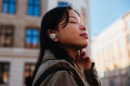 Woman listening with earbuds while standing in city