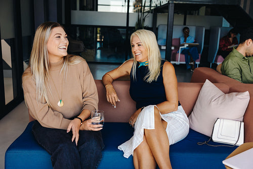 Two women smiling and engaging in conversation on a modern office couch