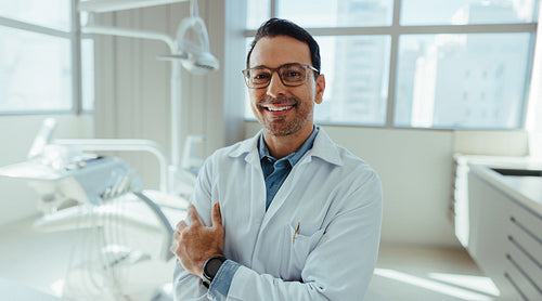 Smiling male dentist crossing arms in modern dental clinic