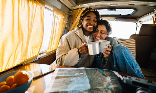 Two friends share cozy moment in camper van with map and mugs