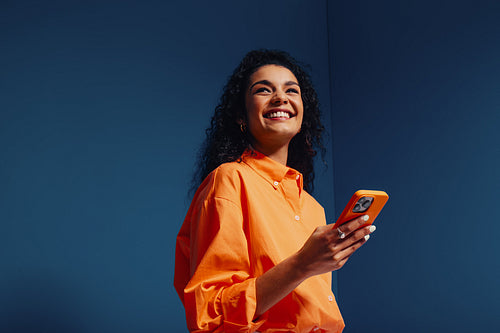 Happy gen z woman using phone in vibrant orange monochromatic setting against blue background