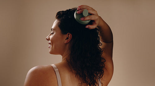 Woman massaging scalp with green brush, smiling in profile