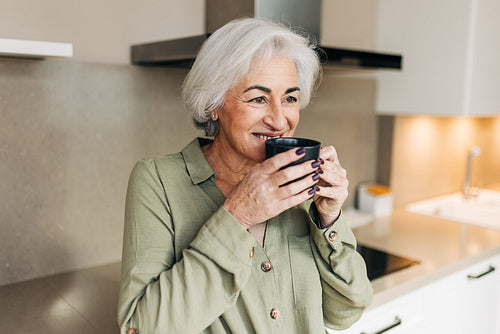 Cheeful elderly woman enjoying a cup of coffee at home