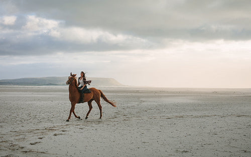 Woman horse riding along the sea shore