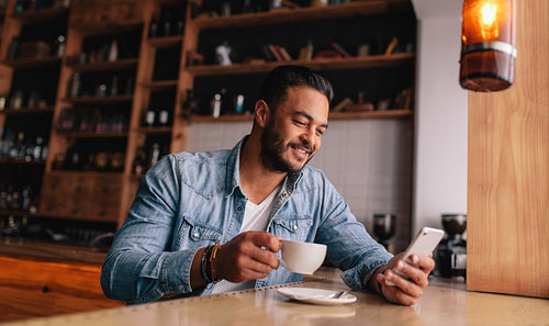 Handsome young man having coffee and using mobile phone