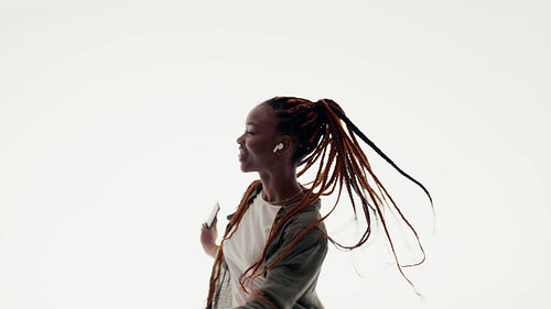 Young African American woman dances freely to music with wireless earbuds in a studio