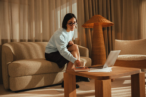 Focused woman works on a laptop with coffee in her home office