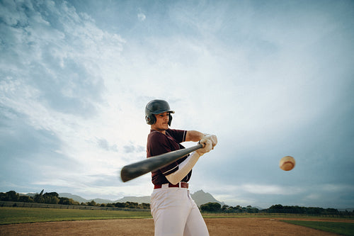 Baseball player intensely swings bat on field under bright sky