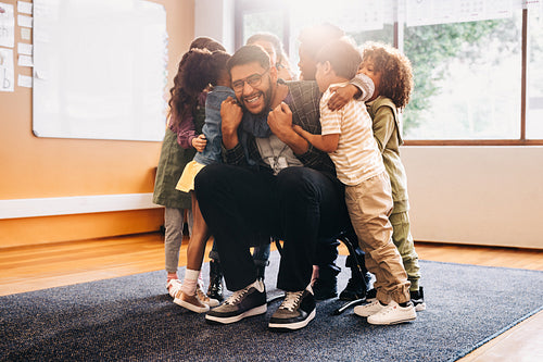 Teacher and students greet each other excitedly. Elementary school educator smiling at the camera as his class embraces him