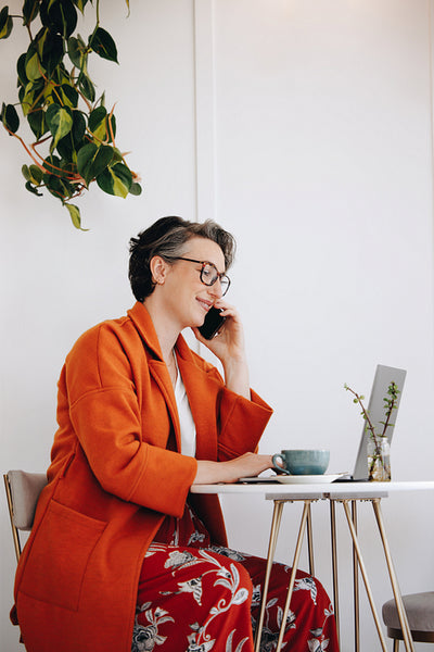 Happy businesswoman taking a phone call while working on a laptop in a cafe