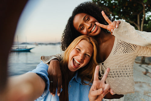 Best friends showing peace signs at the seaside during sunset