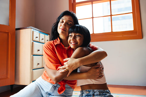 Latina mother and daughter hugging warmly in a cozy home interior