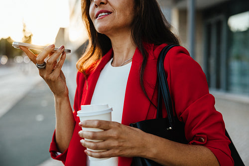 Confident woman in red blazer using smartphone voice assistant outdoors