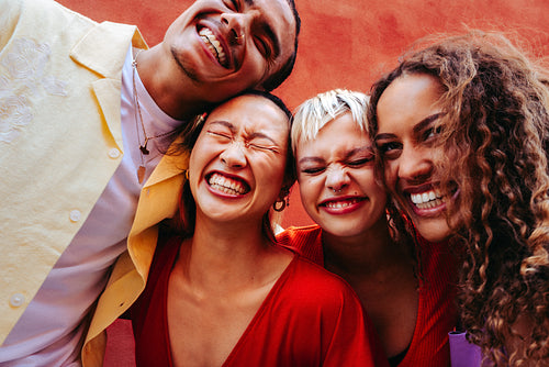 Laughing with friends in a close group against a bold urban wall outdoors